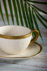 Exclusive expensive tea couple close up against background green plant on tree table. Empty tea cup with saucer with gilded porcelain edges stands on wooden table against background of green palm leaf