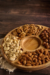 Wooden round plate with various types of nuts, standing on a burlap on the table. Dried cashews, almonds, hazelnuts and walnuts are laid out on a wooden rack