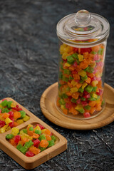 Beautiful colored candied fruit is laid out in a wooden bowl and in a glass jar on the table. Healthy delicious snack of dried fruit on a black textured table in a wooden dish
