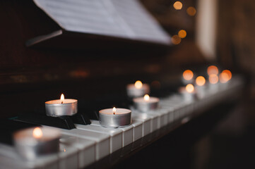 Scented burning candles stay on piano keys closeup. Classic music and romantic atmosphere.
