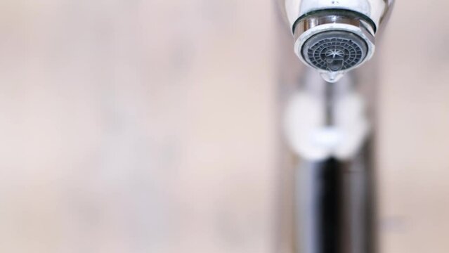 Drop of water drips from the tap. Beautiful fresh and clean water flowing from a tap. Close-up front view slow motion broken chrome faucet in the bathroom. Everyday problems, wasting water and energy.