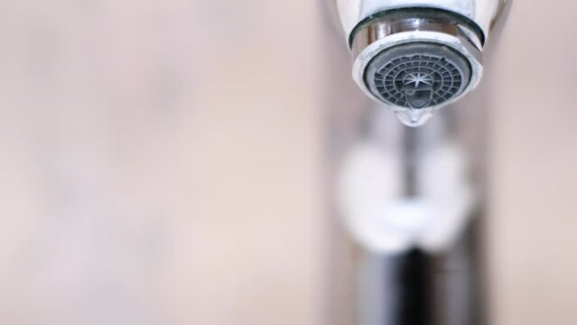 Drop of water drips from the tap. Beautiful fresh and clean water flowing from a tap. Close-up front view slow motion broken chrome faucet in the bathroom. Everyday problems, wasting water and energy.