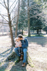 Dad kisses a little girl on his knees sitting on a stump in a flowering meadow
