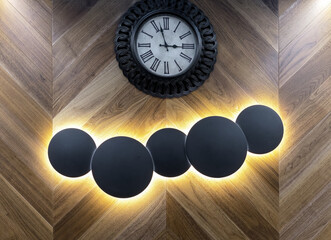 Round illuminated lamps сounter openwork illumination on a wooden wall with a clock.