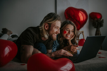 Joyful loving couple looking at laptop and using credit card while shopping online at Valentines day