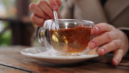 Woman adds sugar to black tea into clear cup at table in cafe. Relaxed woman sweetening tea in cafe...
