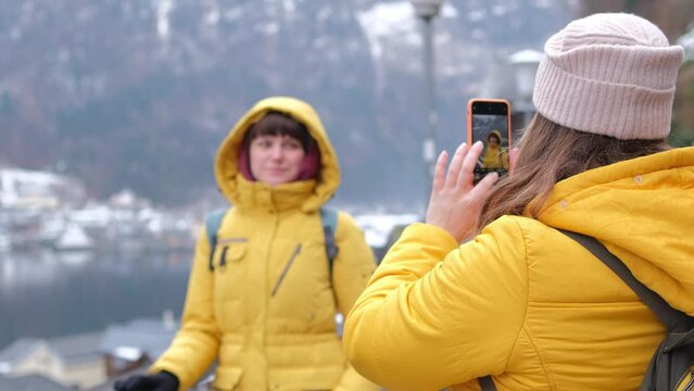 Woman takes pictures of her friend against the backdrop of mountains. Tourists take photos in the Alps. Travelers posing against beautiful nature background. Vacation in winter