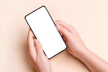 Female hand holding a phone with a blank screen on a beige background - obrazy, fototapety, plakaty
