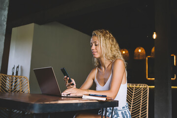 Focused woman browsing smartphone during work on laptop at home