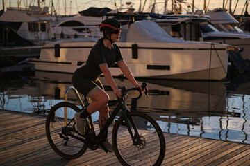 Woman cyclist wearing cycling kit and helmet ,riding a bicycle against the backdrop of a yacht club...