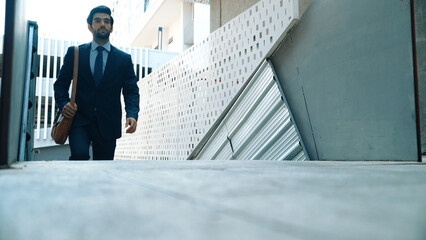 Smart business man walking up the stairs with confident near building. Skilled project manger walking on stairs seeking for job, going for new job near at modern skyscraper. Copy space. Exultant.