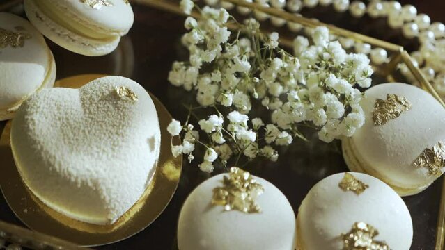 Assorted French macarons on a golden tray
Decorative white flowers accompany the sweets
Luxurious gold leaf detail on pastries
Soft focus background enhances elegance
Romantic, celebratory