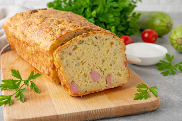 Zucchini bread with cheese, ham and fresh herbs on a wooden board on a gray background. Healthy...