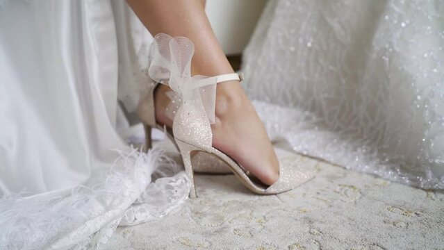 Bride tying shoes with delicate ribbons
Close-up of hands and sparkly heels
Lace dress and feather details visible
Preparing for a wedding ceremony
Elegance and bridal fashion elements