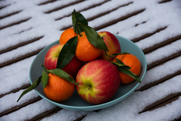 Organic tangerine and apple fruits in bowl on snow covered table in garden. Healthy eating lifestyle background. Energy shot before winter sport activities. Natural Vitamin C snack booster against flu