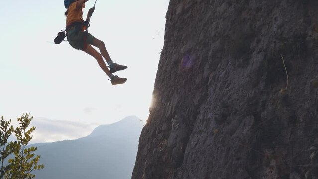 boy is rock climbing. sport in nature. cute teenager goes down on a rope from the mountain. sports people lifestyle concept