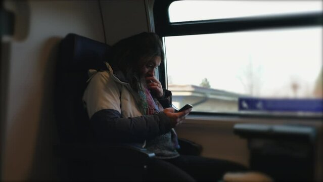 Commuter Using Smartphone on Train with Window View. Female passenger holding phone inside European transportation