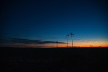 Fototapeta na wymiar Electric poles and lines over farmland at sunset