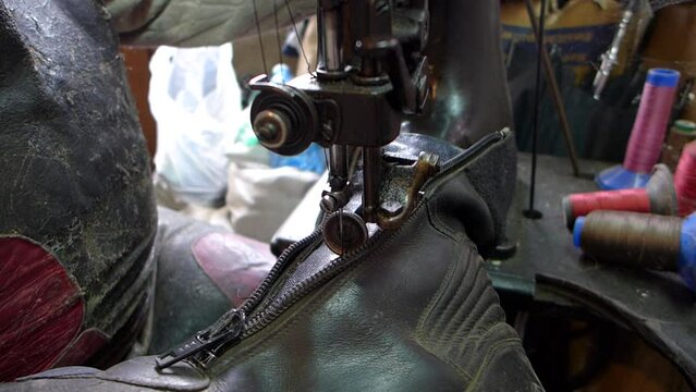 Repair of old shoes at a craftsman specialized in repairing all types of shoes. Close-up of repairing old leather shoes, quilting the zipper on an old sewing machine