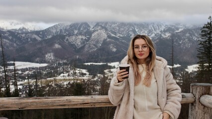 A beautiful girl drinks coffee in a cup against the background of snowy mountains