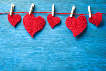 Fototapeta premium Red hearts hanging on a thread with clothespins on a light blue background.