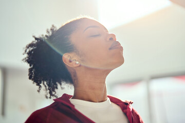 Young healthy fit sporty beautiful African American woman wearing sportswear standing with eyes closed lit with sunlight doing yoga exercises breathing fresh air. Close up. Mental balance concept.