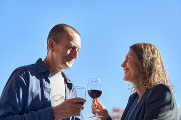 Mature couple on date drinking glass of wine on rooftop on sunny day with copy space