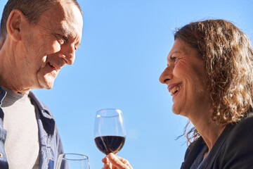 Close up of mature couple on date drinking glass of wine on rooftop on sunny day with copy space