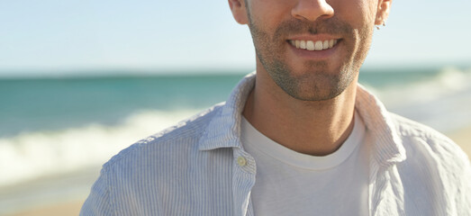 Young handsome confident male smiling and wearing casual shirt at the beack on a sunny day