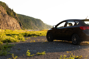 vue sur l'avant d'une voiture noire au bord de la mer avec une falaise en arrière plan lors d'un coucher de soleil en été