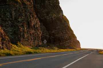 vu sur une route asphaltée droite à deux sens avec des lignes peintes et une falaise en arrière plan lors d'un coucher de soleil doré