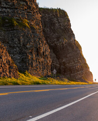 vu sur une route asphaltée droite à deux sens avec des lignes peintes et une falaise en arrière plan lors d'un coucher de soleil
