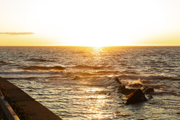 vue sur la mer agitée lors d'un coucher de soleil avec les rayons lumineux et des teintes de jaune...