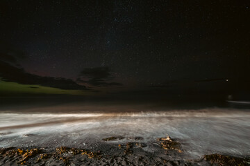 vue sur une plage la nuit avec les premières lueurs d'une aurore boréale dans le ciel