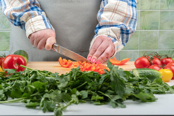Selective focus on female hands cutting sweet pepper with a knife.
