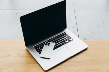 Open laptop with black screen and white smartphone on a wooden surface. Concept of working remotely, online learning, gadgets and devices.