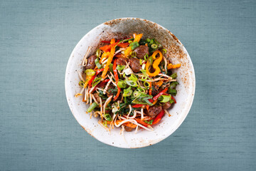 Traditional Asian wok spinach with chestnuts, pepper strips and soy sprouts served as top view in a Nordic design bowl with copy space