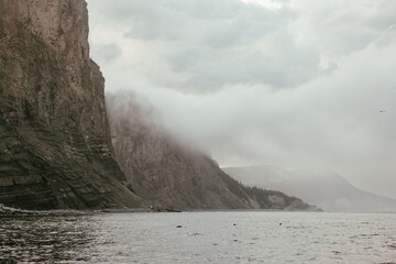 vue sur une paroi rocheuse au bord du fleuve avec le pic dans des nuages bas lors d'une journée d'été brumeuse 