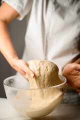 Cook kneads yeast dough with his hands in a glass plate