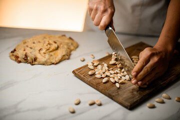 Female pastry chef cuts nuts with a knife on a wooden board
