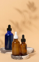 Glass bottles with pipettes on a beige background with a shadow from a branch. Containers for cosmetics