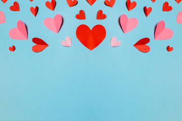 Beautiful pink paper hearts and ribbon arranged on a sky-blue background. Greeting card concept for...