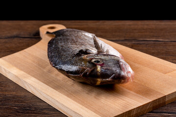 Close-up of raw dorado fish on a cutting board over wooden background.