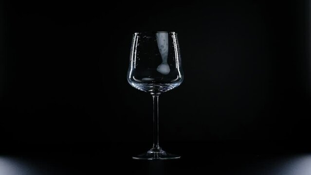 Pouring water into a glass in slow motion on a black background close-up.A drop of water flows down the stem of a glass