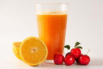 Fresh Organic Acerola and Orange Juice in a glass cup with half orange and acerola berries in a white clean studio photo in front view