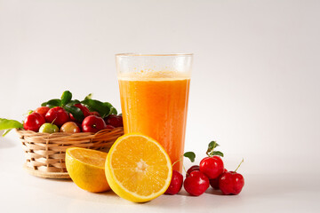 Fresh Organic Acerola and Orange Juice in a glass cup with half orange and acerola berries inside a wood basket in a white clean studio photo in front view