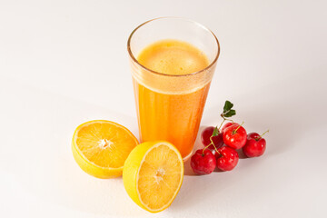 Fresh Organic Acerola and Orange Juice in a glass cup with half orange and acerola berries in a white clean studio photo in top view