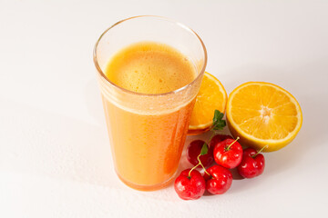 Fresh Organic Acerola and Orange Juice in a glass cup with half orange and acerola berries in a white clean studio photo in top view