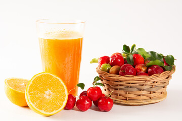 Fresh Organic Acerola and Orange Juice in a glass cup with half orange and acerola berries inside a wood basket in a white clean studio photo in front view