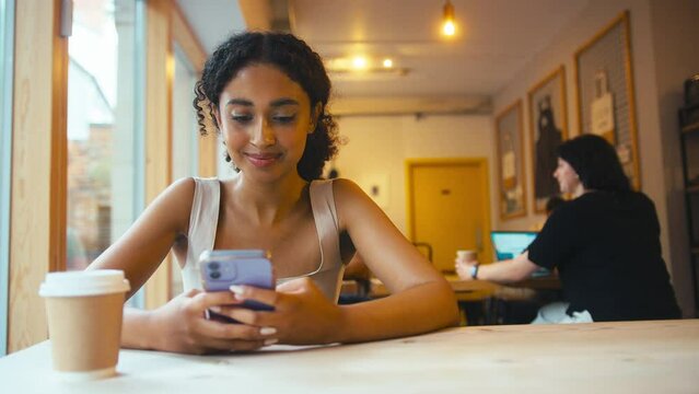 Young woman sitting at table in coffee shop checking social media on mobile phone - shot in slow motion